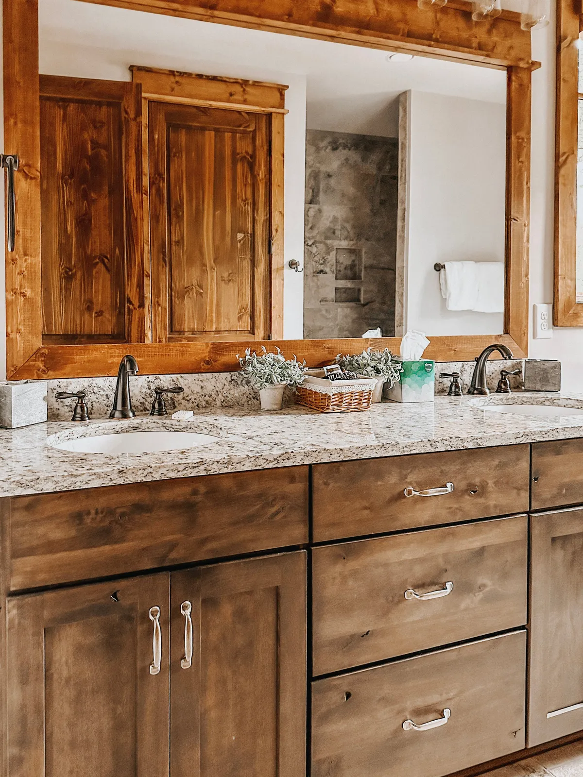 A spa-inspired bathroom with dual granite sinks, wooden cabinetry, and a wide mirror, all softly illuminated by natural morning light. The design exudes calm and encourages self-care routines, echoing the feel of a luxury spa.