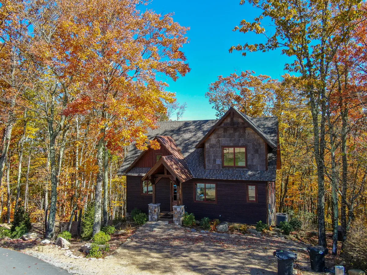 A cozy wooden cabin nestled among colorful autumn foliage, featuring a stone pathway leading toward the porch. The scene hints at the changing seasons and proximity to forest trails, capturing the allure of year-round adventure.