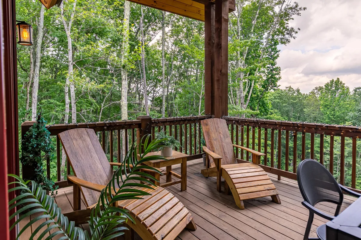 Wooden Adirondack-style lounge chairs are arranged on a deck overlooking abundant greenery. The setup invites guests to relax, read, or socialize, with the surrounding foliage enhancing the sense of seclusion and calm.