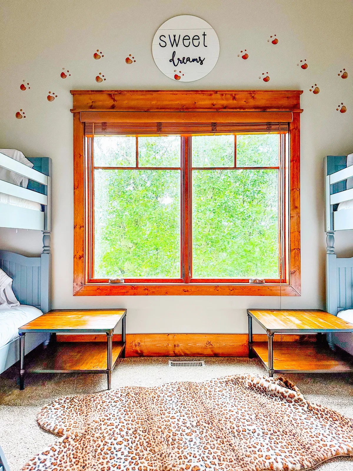 A playful kids' nook featuring bunk beds, a large window for woodland views, and wooden tables ideal for playing games or doing puzzles. Decorative wall art and a serene mood make it inviting for children to hang out, enjoy storytime, or engage in imaginative play.