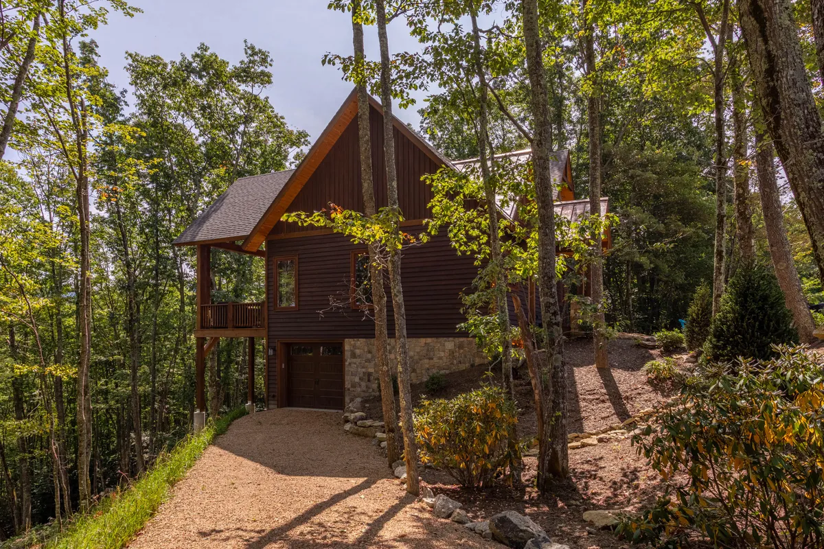 An exterior view of the home surrounded by lush trees, a spacious driveway, and hints of a deck—perfectly capturing the sense of outdoor adventure and natural beauty. The setting suggests plenty of green space for pets to explore and hints at the tranquility of the area.