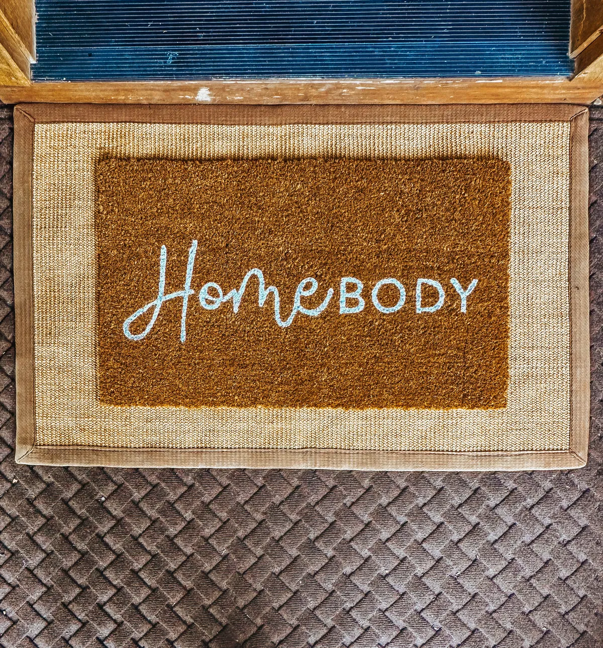 A welcoming entryway with a doormat inscribed with 'HomeBODY,' set on textured flooring. The image evokes the first moments of arrival—stepping inside from an outdoor adventure, with an inviting and homey feel.