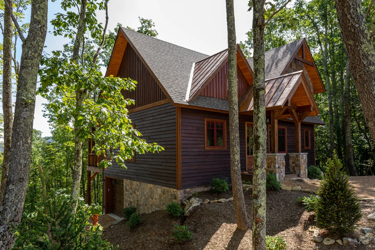 This image shows the wooden exterior of High Country Overlook, grounded by a stone base and surrounded by lush trees. The sloped roof and tranquil garden area reflect the home’s seamless integration with the surrounding environment, hinting at the nearby trailheads and outdoor activities.